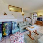 Wohnzimmer mit Kamin, Sofa, Tisch und TV. Holzmöbel und Fenster mit Vorhängen.