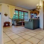 Wohnzimmer mit Sofa, Tisch und Fenstern. Holzgeländer und Kronleuchter sichtbar.