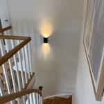 Haus mit Holztreppe und Wandbeleuchtung. Bild zeigt Treppenhaus mit Kunstwerk.