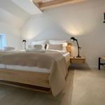 Schlafzimmer mit Holzbett, Nachttisch und Decke. Holzbalken an der Decke.