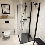 Dusche mit Glaswand, Toilette und schwarzer Sitzbank