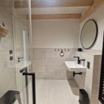 Bad mit Dusche, Waschbecken und runden Spiegel an der Wand.