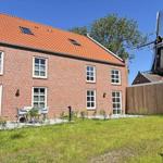 Rotes Ziegelhaus mit Terrasse und Windmühle im Hintergrund.