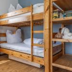 Holz-Etagenbett mit Matratzen, Kissen und Stofftieren. Bücherregal und Heizung sind vorhanden.