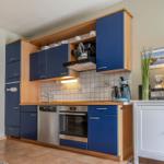 Küche mit blauen Schränken, Spüle, Herd und Kühlschrank.