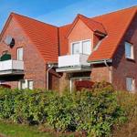 Zwei Wohnhäuser mit rotem Dach und Balkonen, umgeben von grüner Hecke.