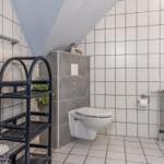 Badezimmer mit Toilette, Waschmaschine und Regal. Dachneigung und Fenster sichtbar.