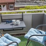 Terrasse mit Tisch, zwei Stühlen und Kissen. Hintergrund: grüne Hecke und Haus.