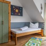 Ein Schlafzimmer mit Dachschrägen, Holzbett, Kleiderschrank und Spielteppich.