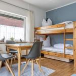 Ein Raum mit Schlafcouch, Tisch und Stühlen. Fenster mit Vorhängen.