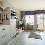 Küche mit Wohnbereich und Balkon mit Blick auf Hochhäuser.