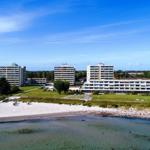 Strandfront mit mehreren Hochhäusern und Grünflächen unter blauem Himmel.