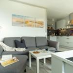 Wohnzimmer mit Sofa, Couchtisch und Küche im Hintergrund.