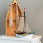 Ein hölzernes Bootmodell mit Rudern und Segeln steht auf einem weißen Tisch.