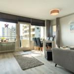 Wohnung mit Essbereich, Sofa und Balkon. Holzboden und Fensterfront.