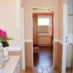 Flur mit Terrakottaboden, Tür zu Schlafzimmer und Bad. Links Küchenzeile mit Blumen.