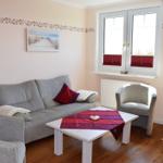 Wohnzimmer mit Sofa, Sessel und Tisch. Fenster mit roten Jalousien.