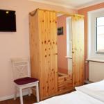 Schlafzimmer mit Bett, Kleiderschrank, Stuhl und Fernseher an der Wand.