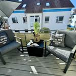 Terrasse mit zwei Sesseln, Tisch und Sonnenschirm. Blick auf Wohnhaus.