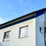 Ferienhaus mit Schild RESIDENZ AM STRAND und Balkonen unter blauem Himmel.