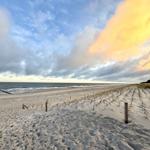 Strand mit Sanddünen und Blick aufs Meer bei Sonnenuntergang.
