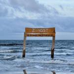 Holzschild Zingst am Strand mit Wellen im Hintergrund.