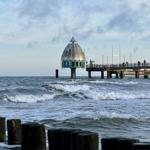 Küstenlandschaft mit Pier und markanter Kuppelstruktur im Hintergrund.