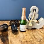 Eine Flasche Sekt, zwei Gläser und ein Anker auf einer Holzoberfläche.