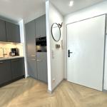 Küche mit grauen Schränken und Holzboden. Hinter dem Eingang steht ein runder Spiegel.