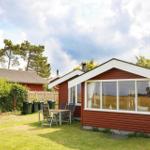 Roter Holzhaus mit Terrasse und Garten. Grünflächen und Bäume im Hintergrund.