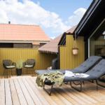 Terrasse mit Liegestühlen, Sitzgelegenheit und Pflanzen an gelbem Holzgeländer.