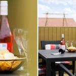 Terrasse mit Tisch, Stühlen, Wein und Chips. Hintergrund: Holzzaun und Dach.