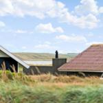 Zwei Häuser mit Dächern, umgeben von Gras und einem Feld unter blauem Himmel mit Wolken.