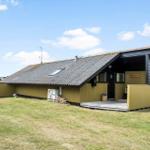 Holzhaus mit grünem Zaun und Holzstapel im Garten unter blauem Himmel.