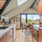 Küche mit Essbereich, Holzboden und großem Fenster mit Blick auf die Landschaft.