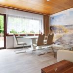 Esszimmer mit Tisch, Stühlen und Blick auf Garten. Wandbild zeigt Strand.