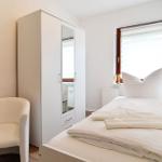 Ein Schlafzimmer mit weißem Bett, Kleiderschrank und Sessel. Fenster mit Jalousie.