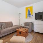 Wohnzimmer mit Sofa, Sessel, Fernseher und Holzkiste.