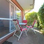 Terrasse mit zwei Liegestühlen und Tisch. Durchgehende Glastüren zum Innenraum.