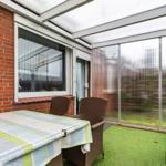 Terrasse mit Tisch, Stühlen und künstlichem Gras unter transparentem Dach.