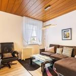 Wohnzimmer mit Sofa, Sessel, Glas-Tisch und Holzdecke.