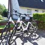 Zwei weiße E-Bikes stehen vor einem Haus mit grünem Heck.
