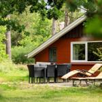 Rotes Holzhaus mit Terrasse, Tisch, Stühlen und Liegestühlen im Grünen.
