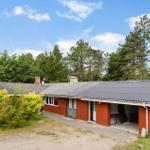 Rotes Haus mit Garage und Garten, umgeben von Bäumen unter blauem Himmel.