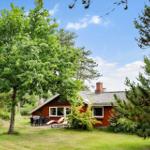 Rotes Haus mit Garten, Terrasse und Gartenmöbeln unter Bäumen.