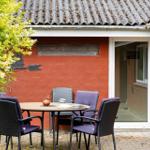 Roter Hauswände mit Terrasse, Tisch und Stühlen. Pflanzen und Dachziegel sind sichtbar.