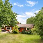 Rotes Haus mit Garten, Terrasse und Grillplatz unter Bäumen.