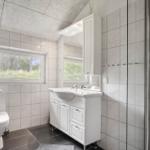 Badezimmer mit Toilette, Waschbecken und Dusche. Fenster mit Blick auf Grün.