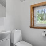 Badezimmer mit Toilette, Waschbecken und Fenster zum Wald.