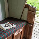 Holzbank mit gestreifter Sitzfläche und offenes Buch mit Brille.